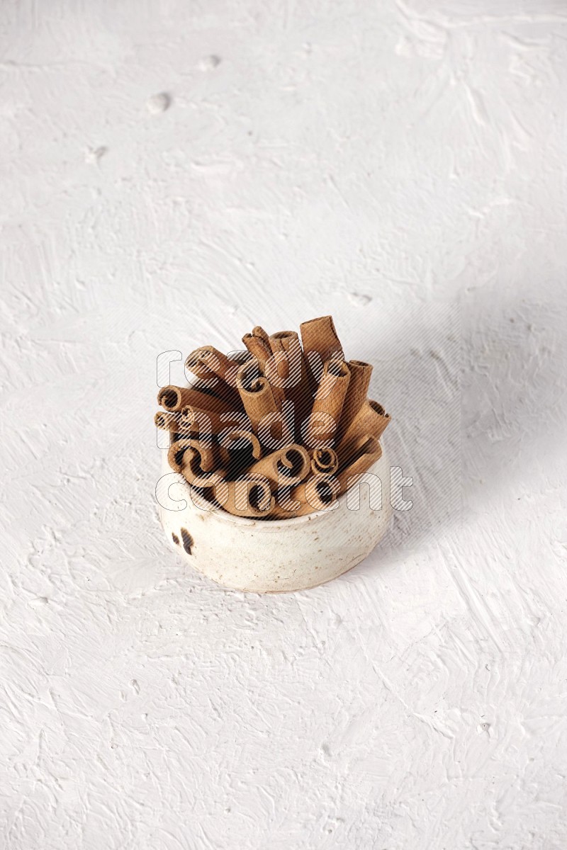 Cinnamon sticks in a beige bowl on a white background