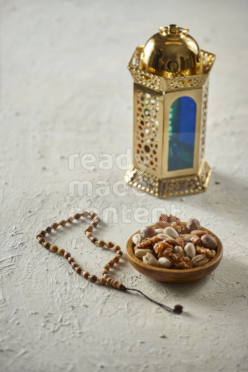 A golden lantern with different drinks, dates, nuts, prayer beads and quran on textured white background