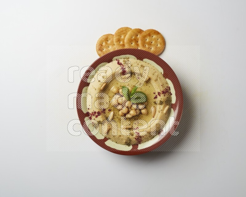 Hummus in a traditional plate garnished with zaatar & sumak on a white background
