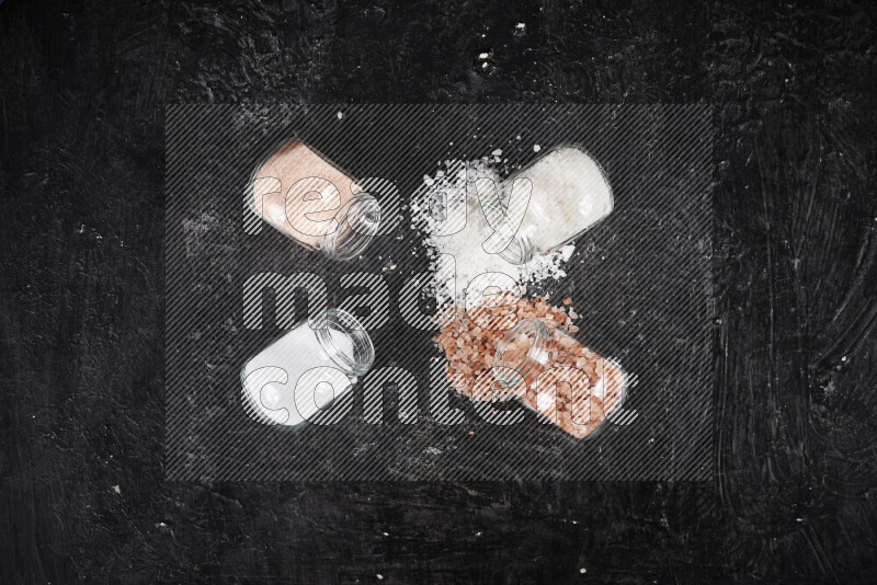 4 glass jars filled with table salt, coarse sea salt, fine himalayan salt and coarse himalayan salt on black background