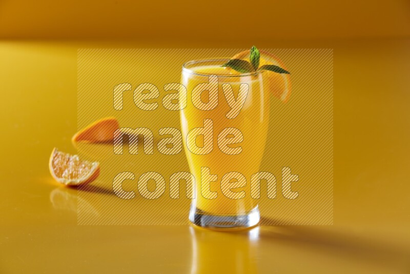 glass of orange juice with orange & mint  on yellow background