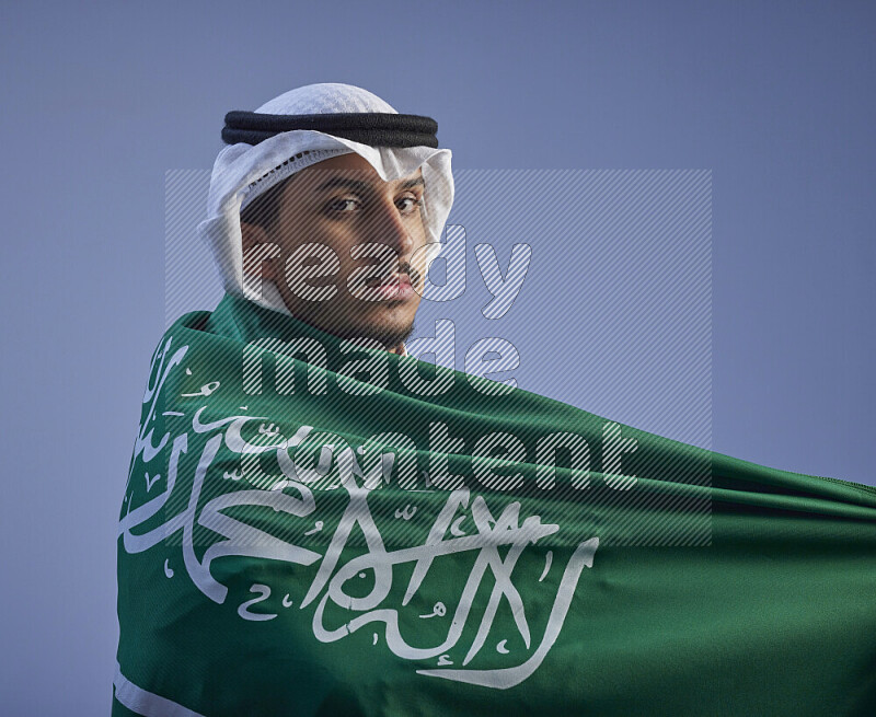 رجل سعودي يرتدي ثوب وشماغ ابيض يلف علم سعودي كبير على كتفه