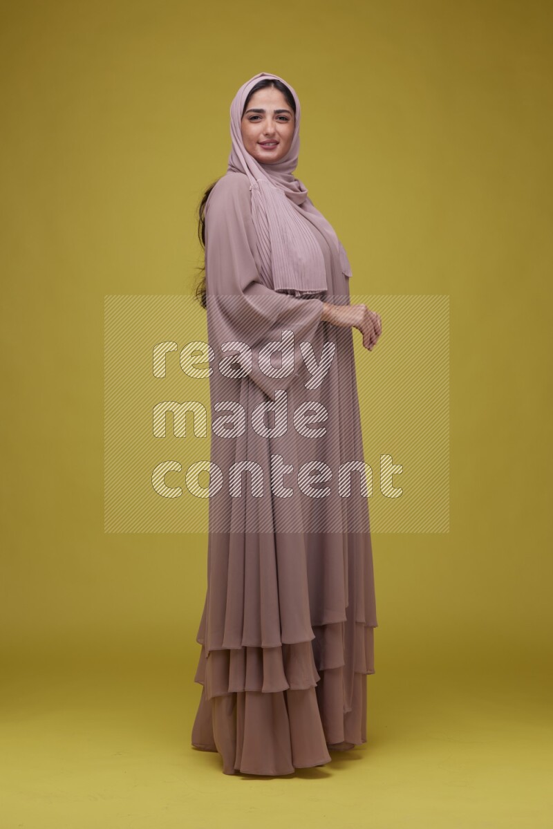 A woman Posing on a Yellow Background wearing Brown Abaya with Hijab
