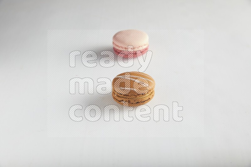 45º Shot of of two assorted Brown Irish Cream, and Pink Litchi Raspberry macarons on white background