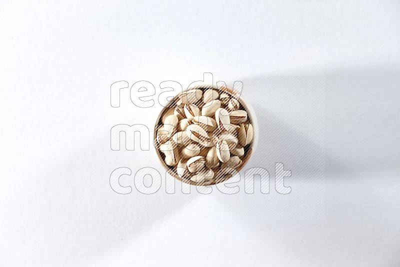 A beige ceramic bowl full of pistachios on a white background in different angles