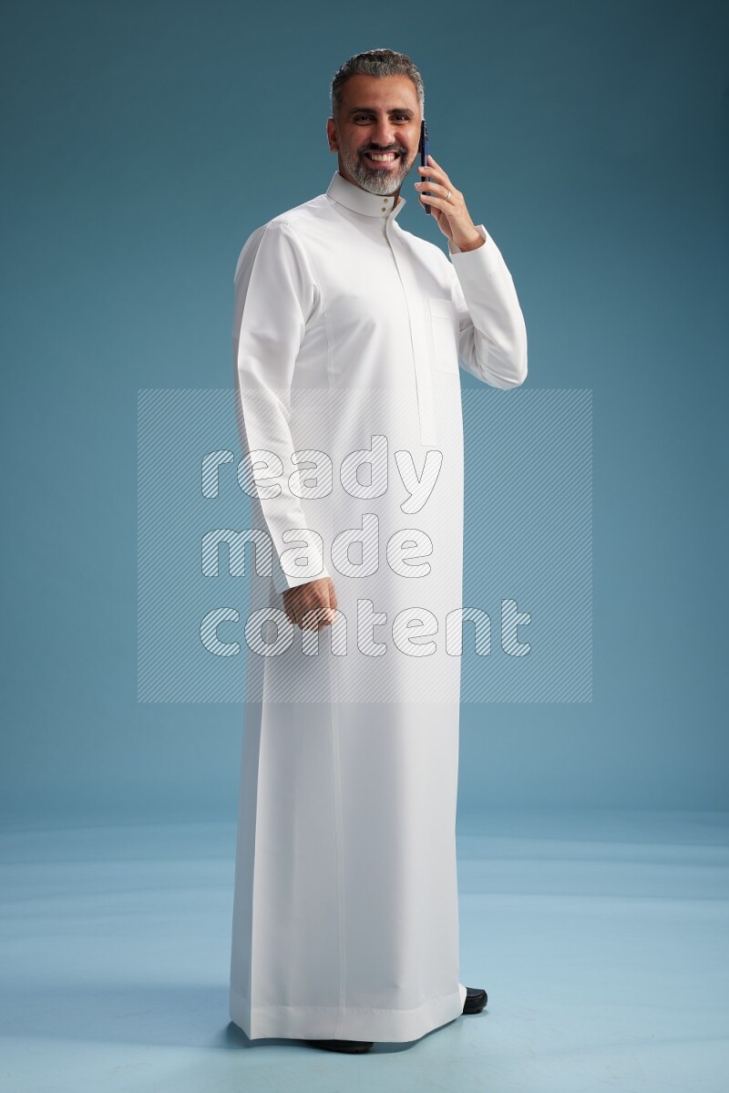 Saudi man wearing thob talking on the phone on blue background