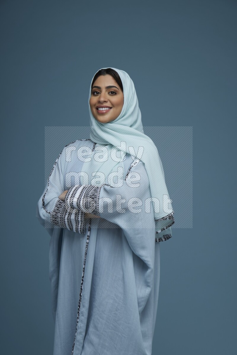 A woman posing in a blue background wearing a blue Abaya with hijab