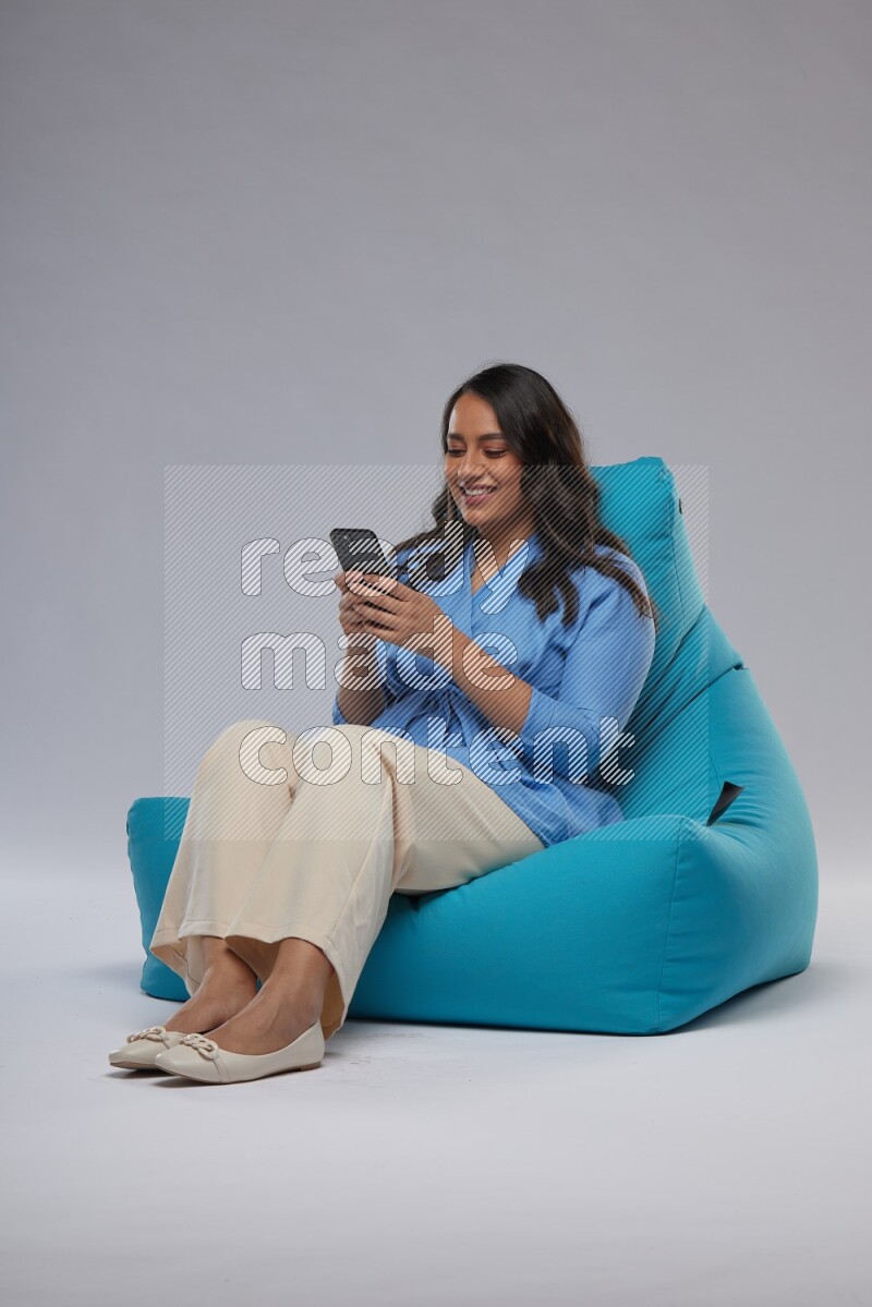 A woman sitting on a blue beanbag and texting on phone