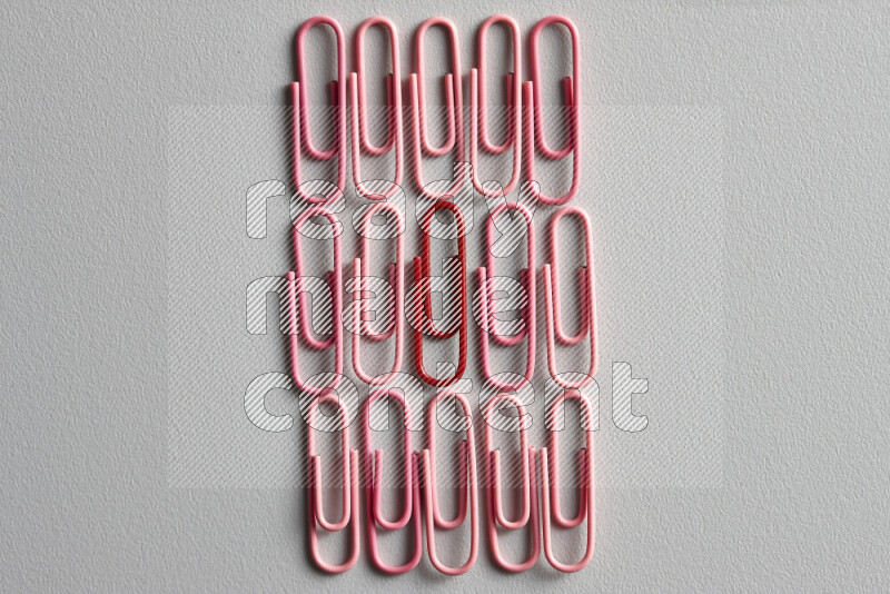 A bunch of pink paper clips with a different colored paper clip in the center on grey background