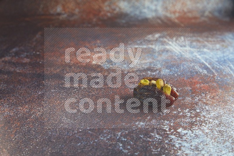 one pistachio stuffed madjoul date on a rustic reddish background
