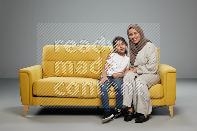 A girl with her mother sitting and interacting with the camera on gray background
