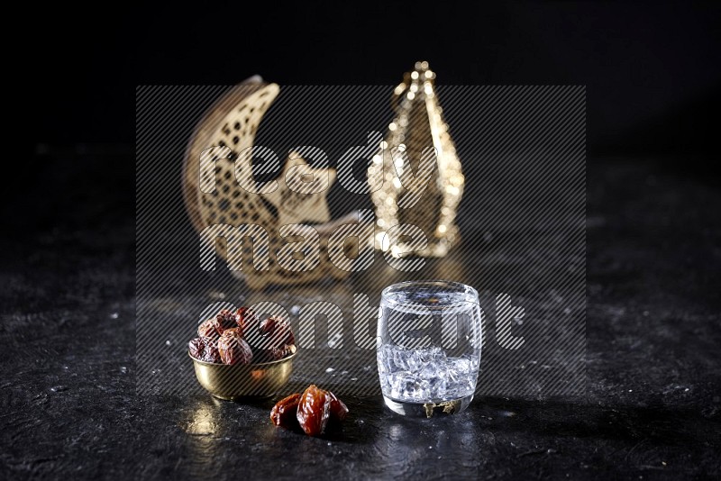 Dates in a metal bowl with water beside golden lanterns in a dark setup