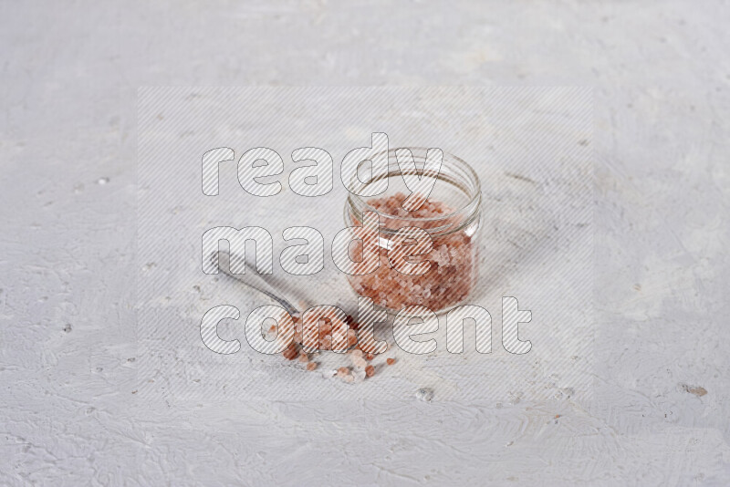 A glass jar full of coarse himalayan salt crystals on white background