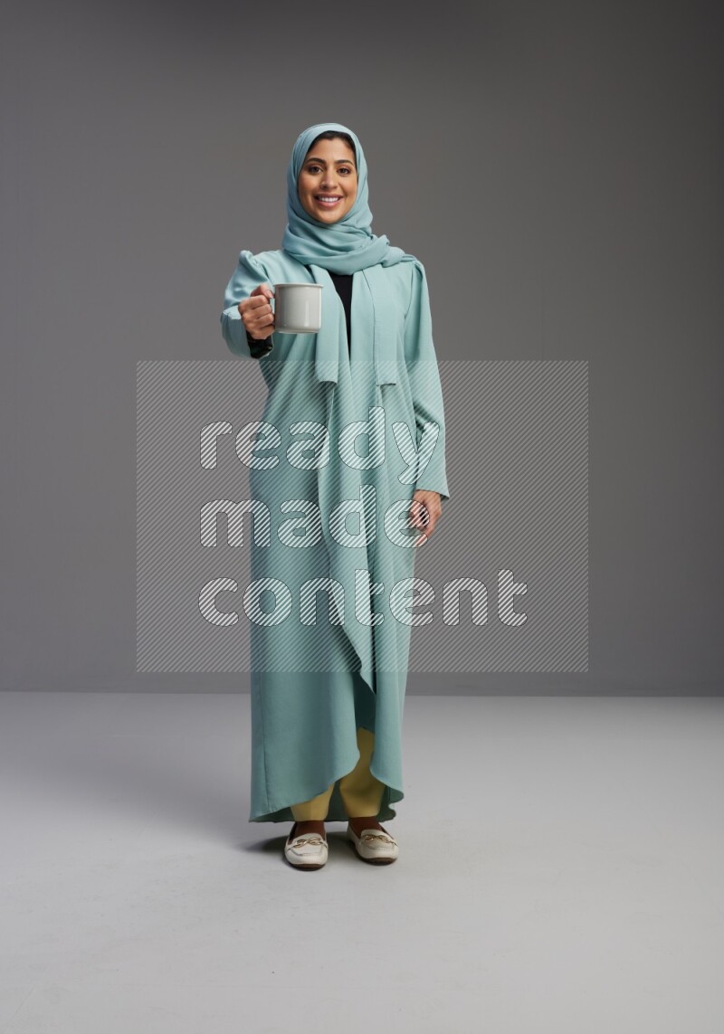 Saudi Woman wearing Abaya standing  holding a mug on Gray background