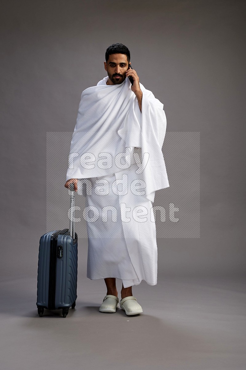 A man wearing Ehram Standing holding traveling bag on gray background