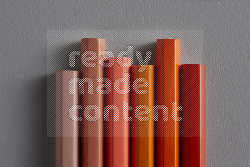 A collection of colored pencils arranged showcasing a gradient of orange hues on grey background