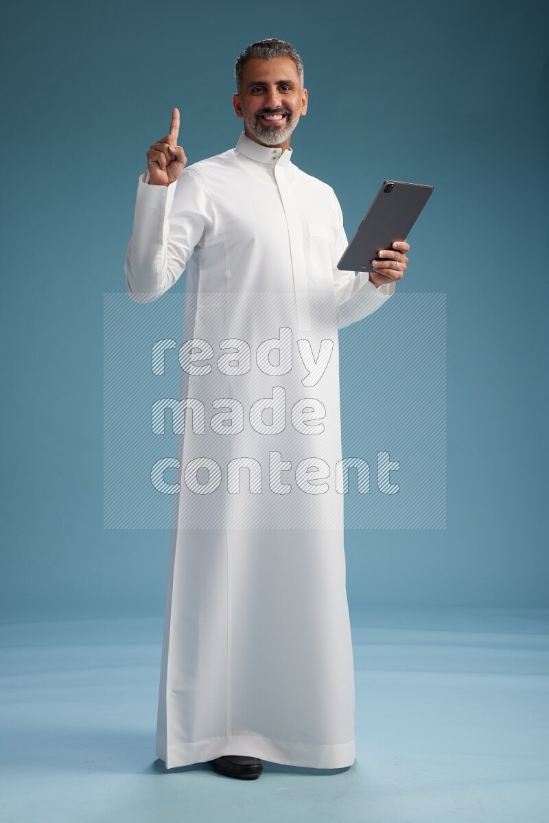 Saudi man waring thob with tablet on blue background