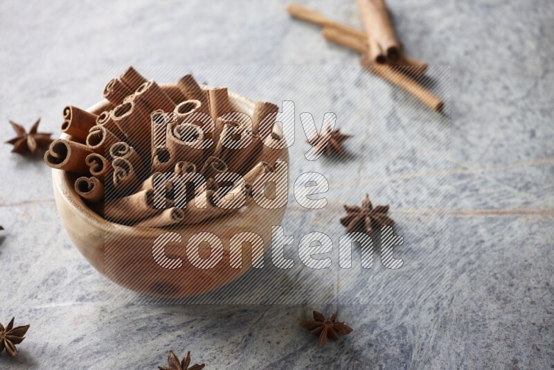 wooden bowl full of cinnamon sticks surrounded by star anis on marble background in different angles