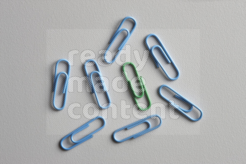 A bunch of blue paper clips with a different colored paper clip in the center on grey background