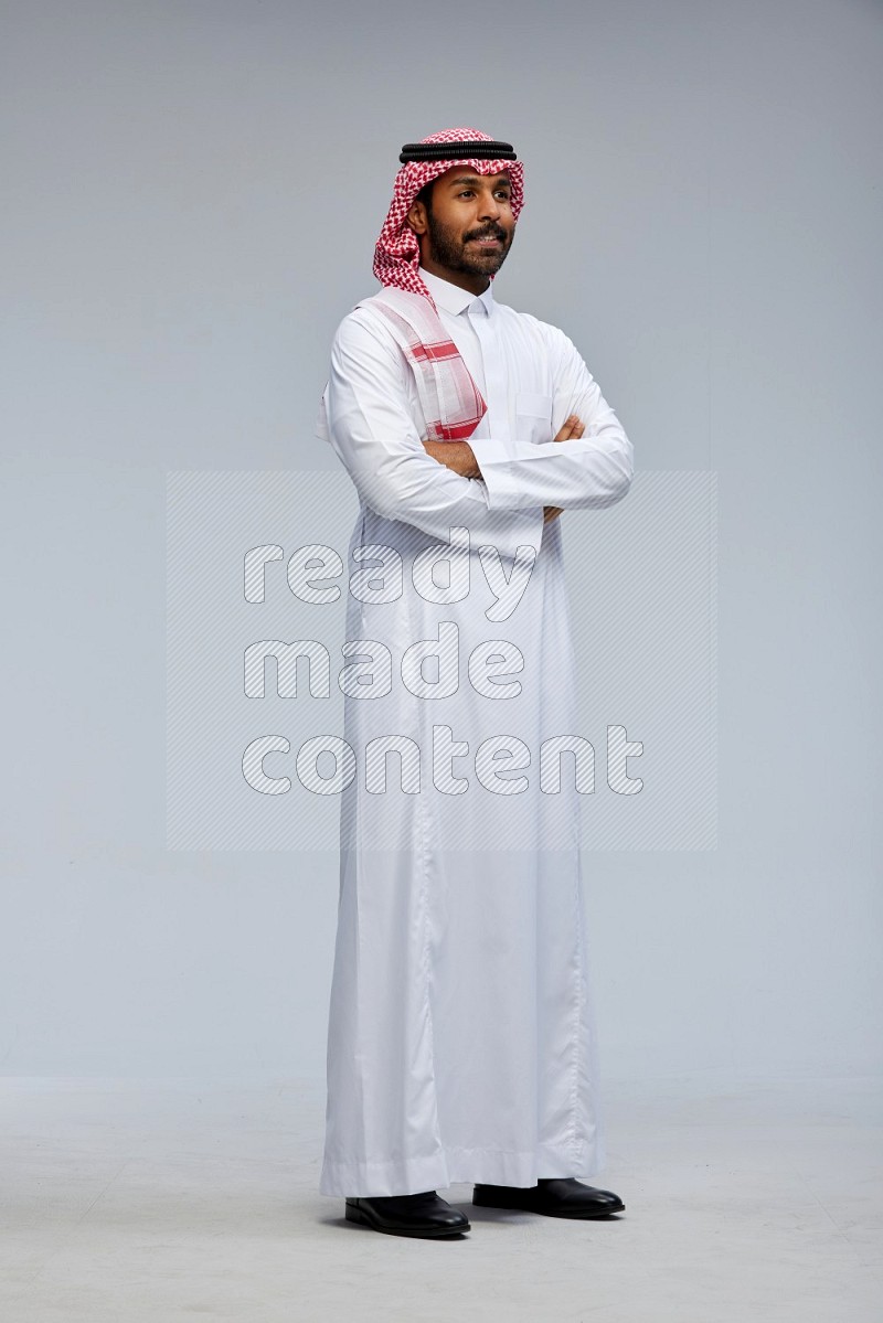 Saudi man Wearing Thob and shomag standing with crossed arms on Gray background