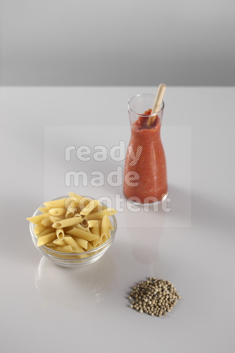 Raw pasta with tomatoe pasta with different ingredients such as cherry tomatoes, basil, garlic, bay laurel, cardamom, white pepper, black pepper, red chilis and wheat stalks on light grey background