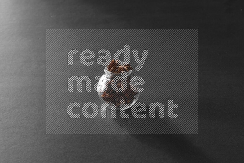 A glass spice jar full of star anise on black flooring