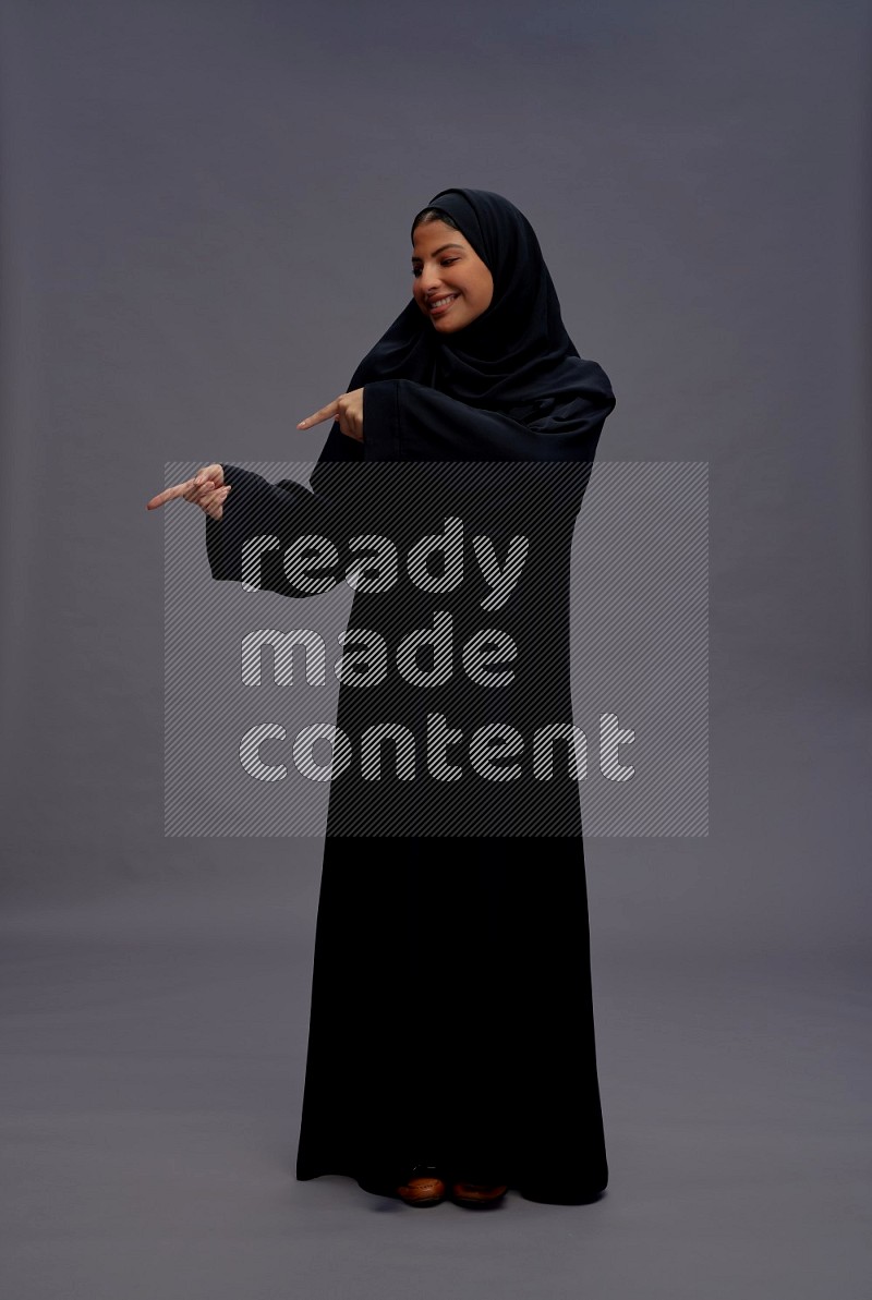 Saudi woman wearing Abaya standing interacting with the camera on gray background