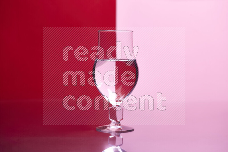 The image features a clear glassware filled with water, set against red and rose background