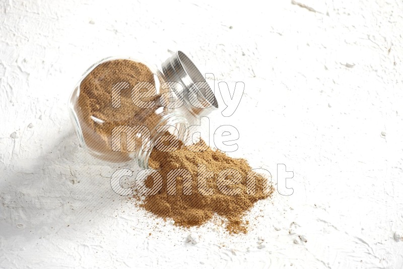 Flipped glass jar full of cinnamon powder on a textured white background