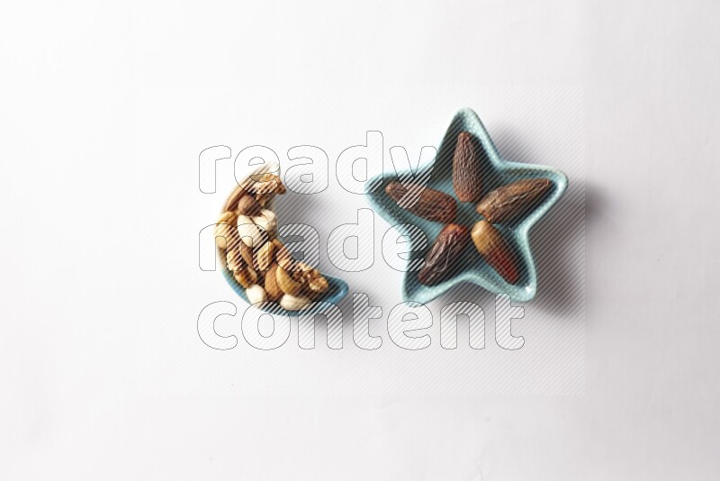 Dates in a star shaped pottery plate and a crescent plate with mixed nuts on white background