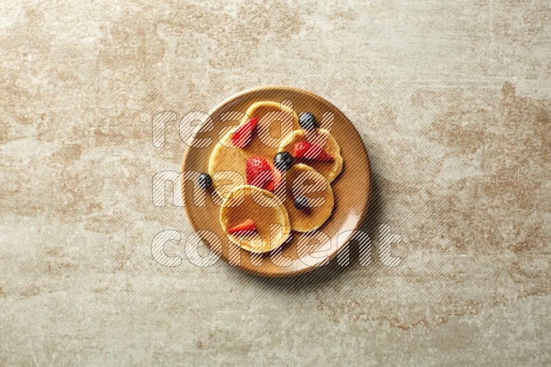 Five stacked mixed berries mini pancakes in a brown plate on beige background