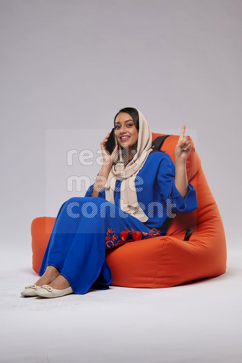 A Saudi woman wearing Jalabiya sitting on an orange beanbag and talking on the phone