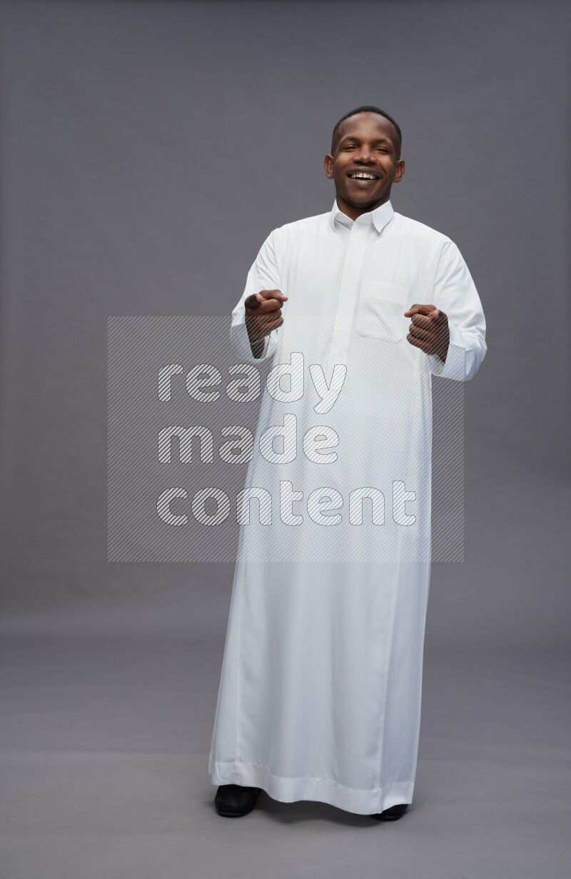 Saudi man wearing thob standing interacting with the camera on gray background
