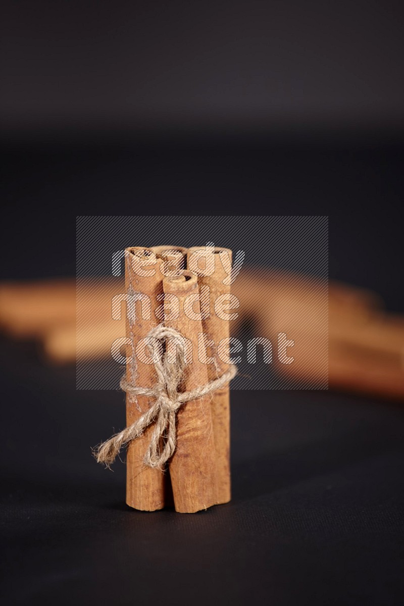 4 Cinnamon sticks stacked and bounded with more sticks in the background on black flooring