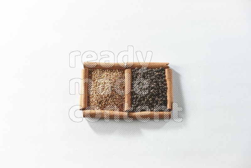 مربعان من أعواد القرفة ممتلئان بحبوب الخردل وحبوب الفلفل الأسود علي خلفية بيضاء