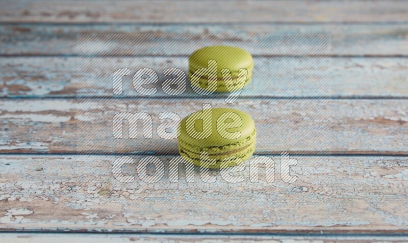45º Shot of two Green Pistachio macarons on light blue wooden background