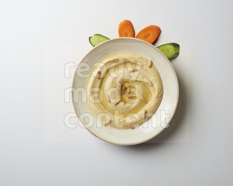 Hummus in a pottry plate garnished with pine nuts on a white background