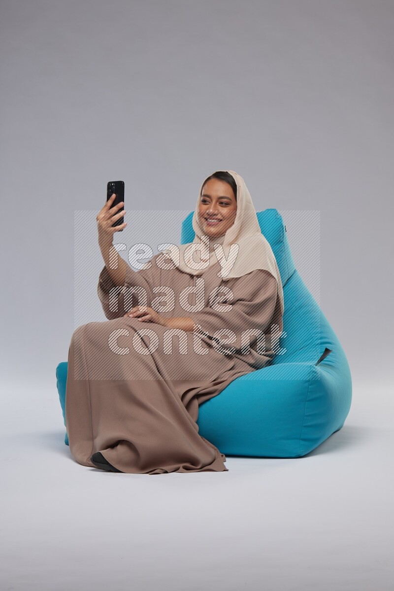 A Saudi woman sitting on a blue beanbag and taking selfie