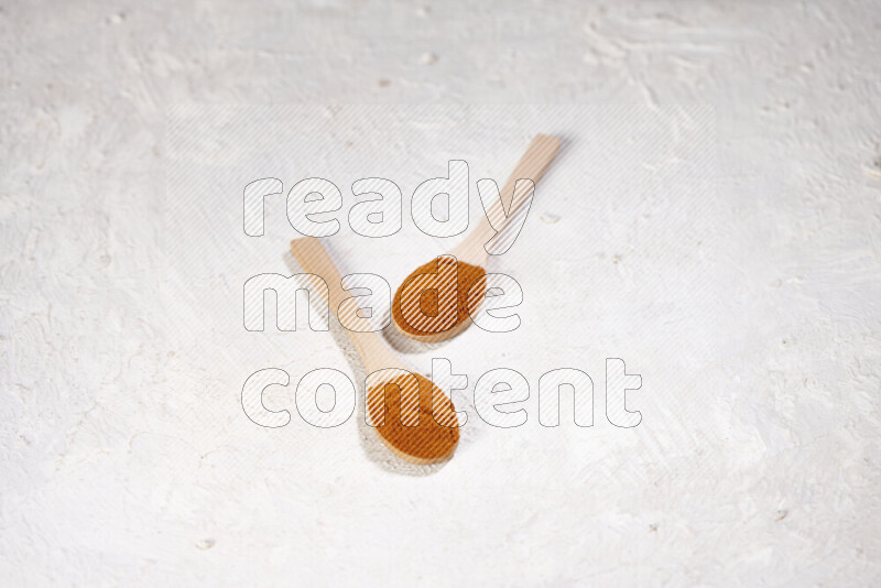 Two wooden spoons full of ground paprika powder on white background