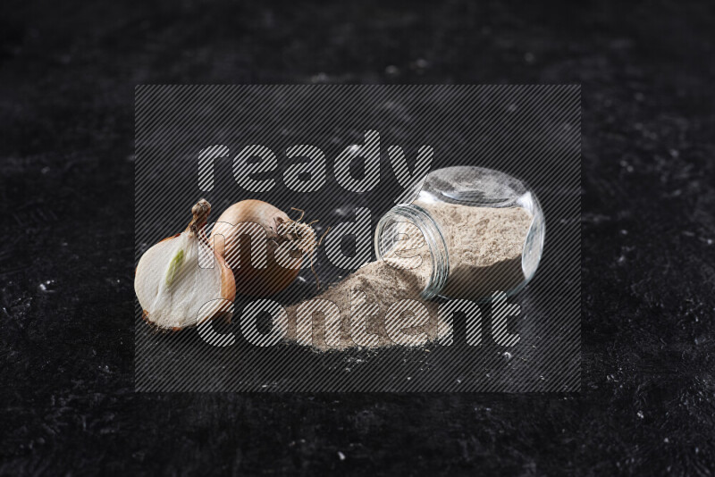 A glass jar full of onion powder flipped with some spilling powder on black background