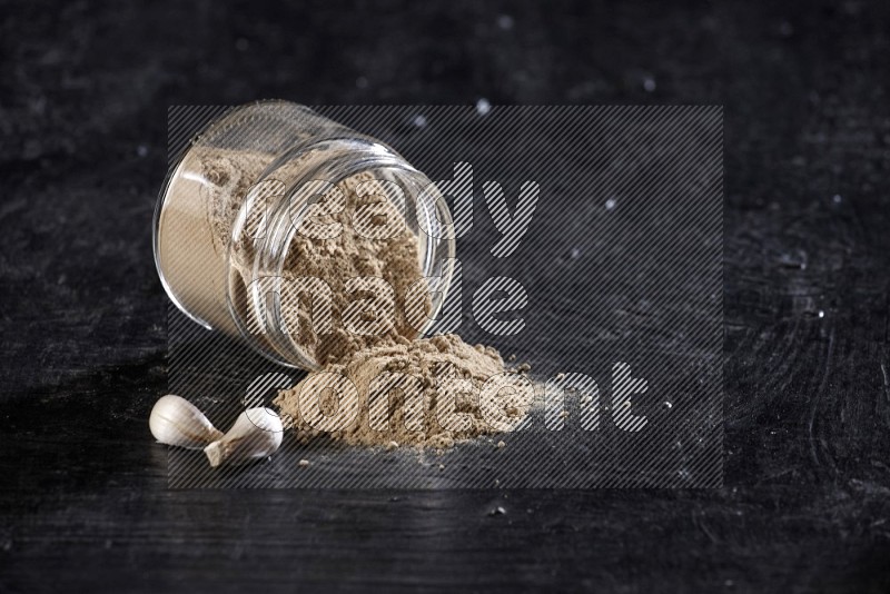 A glass jar full of garlic powder flipped and the powder came out on a textured black flooring in different angles