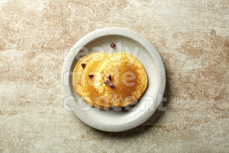 Three stacked chocolate chips pancakes in a grey plate on beige background