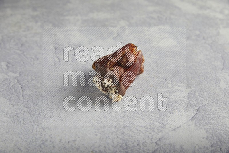 Hazulnut stuffed date covered with dark chocolate and crushed peanuts on light grey background