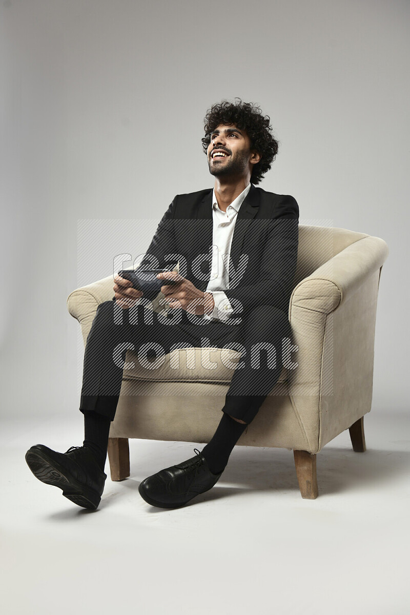 A man wearing formal sitting on a chair gaming on the phone on white background