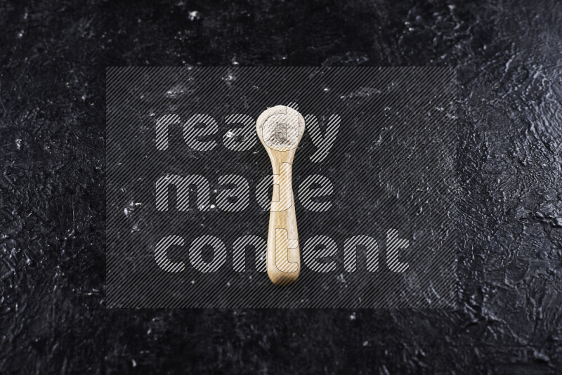 A wooden spoon full of onion powder on black background