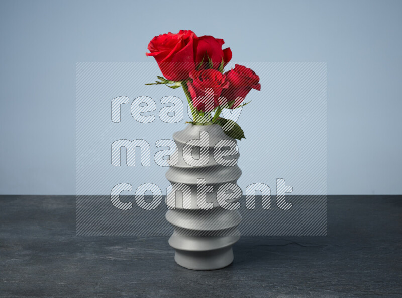 An arrangement of vivid red roses in a grey spiral vase on black marble background