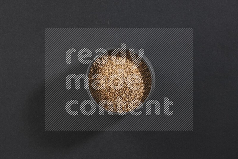 A black pottery bowl full of mustard seeds on black flooring