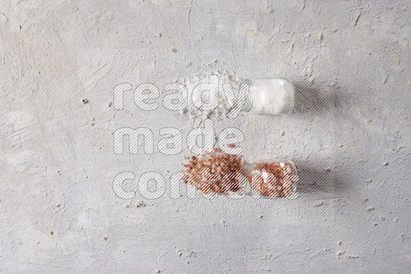 2 glass jars one is filled with coarse himalayan salt and the other with coarse sea salt on white background