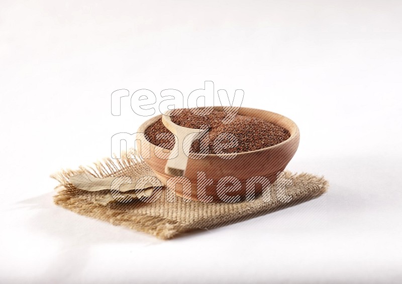 وعاء خشبي وملعقة خشبية كلاهما ممتلئان ببذور حب الرشاد علي قطعة من القماش علي خلفية بيضاء