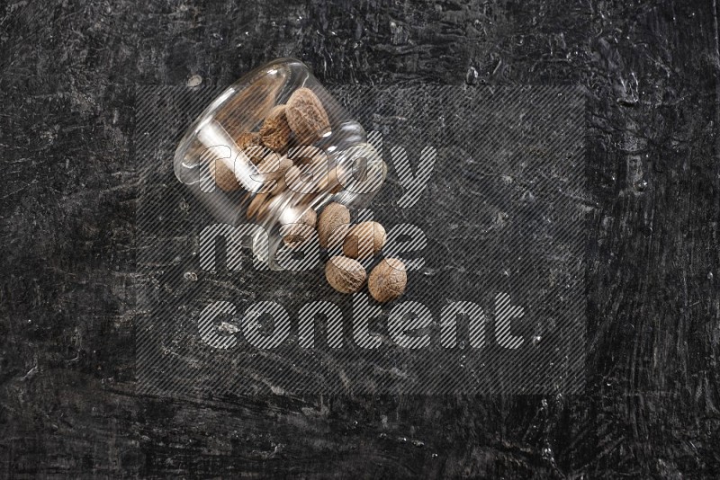 A glass jar full of nutmeg flipped and the seeds came out on a textured black flooring in different angles